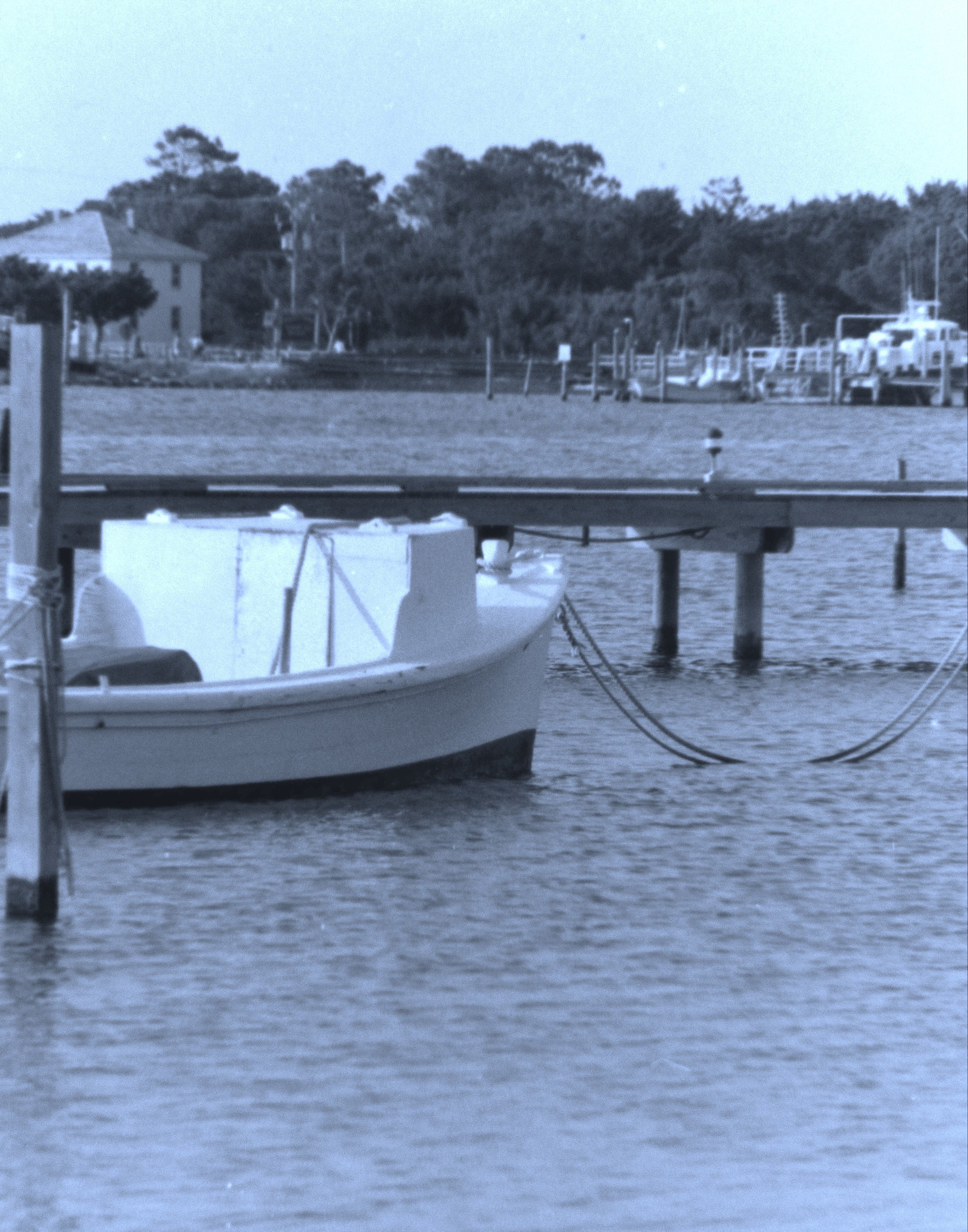 Boat tied to a dock with trees and another boat in the background